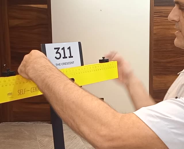 Centering a room 311 sign on the yellow Self-Centered tool using the back ruler